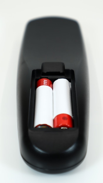 Schwarze TV-Fernbedienung mit AAA-Alkalibatterien in Rot und Weiß auf weißem Hintergrund. Batteriewechsel, Ersatzteile. Nahaufnahme des Batteriefachs der Fernbedienung. Vertikale Fotografie.