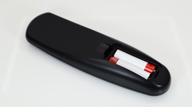 Schwarze TV-Fernbedienung mit AAA-Alkalibatterien in Rot und Weiß auf weißem Hintergrund. Batteriewechsel, Ersatzteile. Nahaufnahme des Batteriefachs der Fernbedienung.