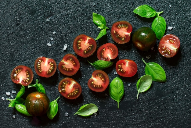 Schwarze und rote Kirschtomaten des Lebensmittelhintergrundes und grüner Basilikum auf einer Draufsicht des nassen Steinhintergrundes