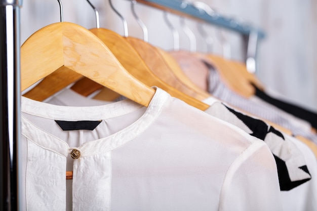 Schwarze und weiße Frauenkleider auf hölzernen Kleiderbügeln auf einem Gestell in einem Modegeschäft. Schrank Geschäftsfrau