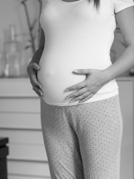 Schwarze und weiße schöne schwangere Frau im weißen T-Shirt, die dicken Bauch berührt