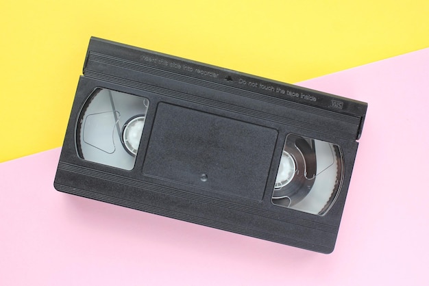 Schwarze VHS-Videokassette auf gelbem und rosafarbenem Hintergrund. Alte veraltete Technologie für Tonbandaufnahmen