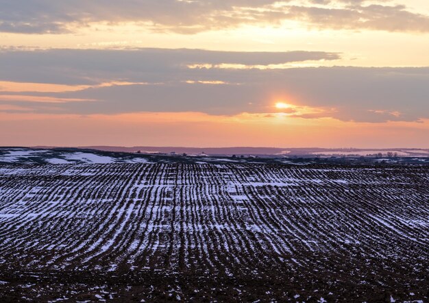 Schwarzer Ackerland mit dem letzten Schnee im frühen Frühling Ruhe am Abend Sonnenuntergang im ländlichen Lviv-Gebiet der Ukraine