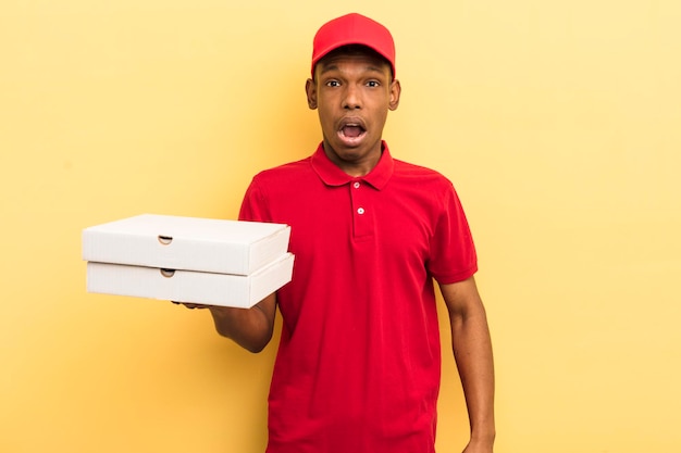Schwarzer afro junger Mann, der sehr schockiert oder überrascht aussieht Pizzabote Konzept