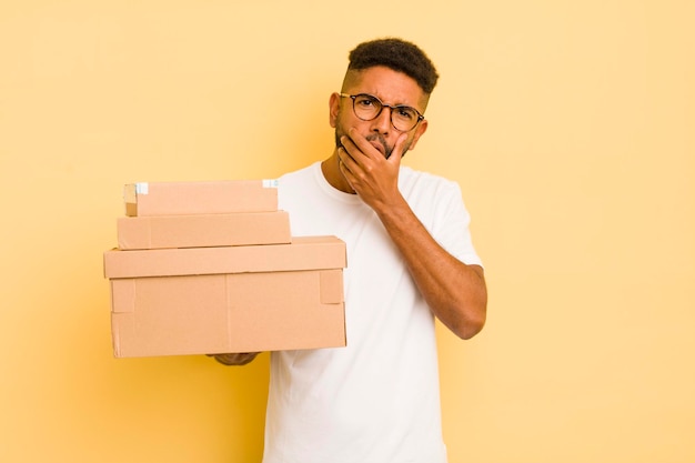 Schwarzer Afro-Mann mit weit geöffnetem Mund und Augen und Hand am Kinn Versandkartons Konzept