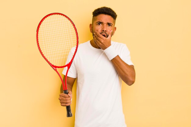 Schwarzer Afro-Mann mit weit geöffnetem Mund und weit geöffneten Augen und Hand auf Kinn-Tennis-Konzept