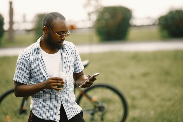 Schwarzer amerikanischer Mann, der auf einem Gras steht und ein Telefon benutzt. Mann mit weißem T-Shirt und blauem kariertem Hemd