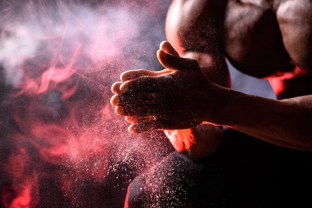 Schwarzer Bodybuilder verwendet Handmagnesia Ein Mann sitzt auf einem schwarzen Hintergrund mit rotem Rauch