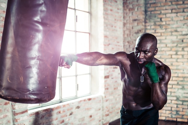 Schwarzer Boxer, der die schwere Tasche im Fitnessstudio schlägt