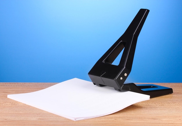 Schwarzer Bürolocher mit Papier auf blauem Hintergrund