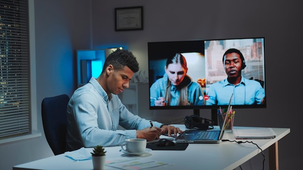 Schwarzer Chefmanager, der einen Videoanruf auf einem großen Monitor mit Kollegen in Quarantäne macht, die zu Hause arbeiten...