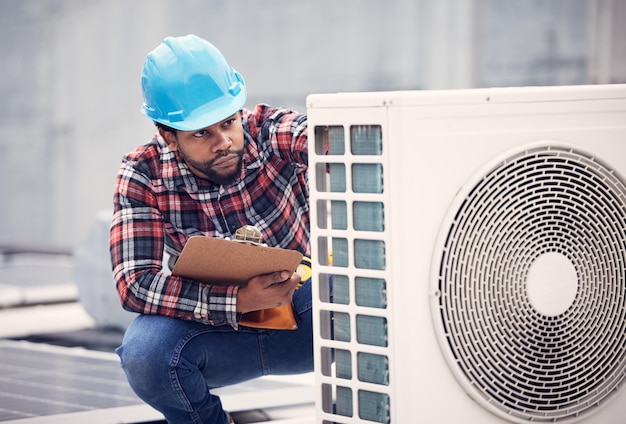 Schwarzer Elektriker mit Klemmbrett für die Inspektion der Klimaanlage. Handwerker arbeitet auf dem Dach mit Fokus auf Wartungsprüfung, AC-Reparatur und männlicher Techniker mit Stromgenerator und Service