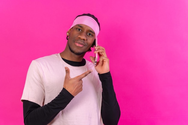 Schwarzer ethnischer Mann mit einem Telefon in rosafarbener Kleidung auf einem rosafarbenen Hintergrund, der auf das Telefon zeigt