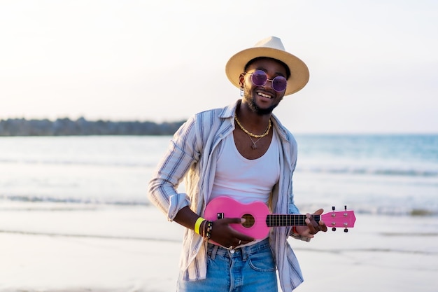 Schwarzer ethnischer Mann spielt Ukulele am Meer und genießt die Sommerferien