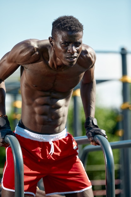 Schwarzer Fitness-Mann, der Dips ausübt, Cross-Training des männlichen Modells in der städtischen Umgebung. Ein Afrikaner in den Zwanzigern trainiert auf der Straße.