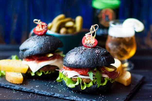 Schwarzer Hamburger mit Rindfleisch, Salat und Pommes Frites. Frisches Bier in einem Glas. Trends bei Streetfood. Ein Kalorienessen. Kopieren Sie Platz