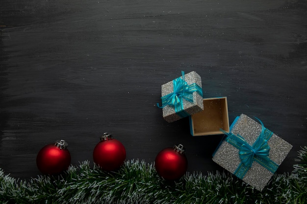 Schwarzer hölzerner Weihnachtshintergrund mit roten Kugeln und Geschenken mit blauer Schleife