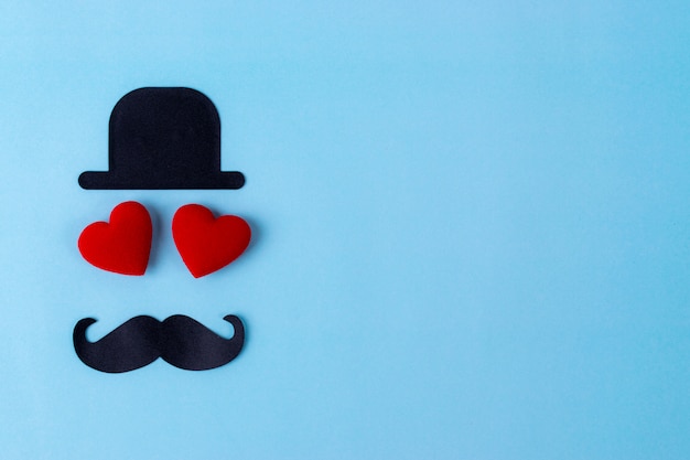 Schwarzer Hut, Schnurrbart und Herz mit zwei Rottönen mit blauem Pastellhintergrund.