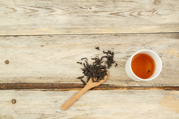 Schwarzer indischer natürlicher Tee auf einem Löffel und in einem Glas auf einem hölzernen Hintergrund gebraut.