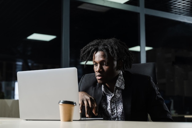 Schwarzer IT-Programmierer arbeitet im Coworking Space am Laptop. Schöner afrikanischer Mann mit Laptop im Büro.