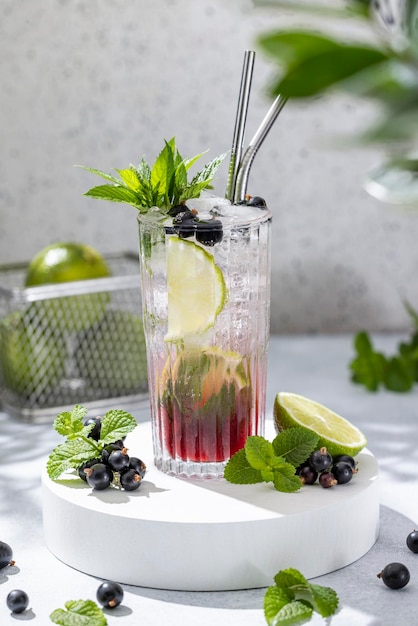 Schwarzer Johannisbeer-Mojito-Cocktail. Elegantes Glas gefüllt mit Cocktails oder Mocktails, umgeben von Zutaten auf grauer Tischoberfläche. Bereit zum Trinken