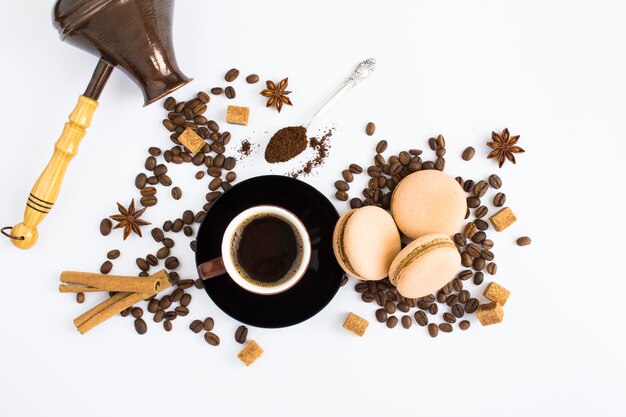 Schwarzer Kaffee in der braunen Tasse, Macarons, Kaffeebohnen und Türken auf weißem Hintergrund