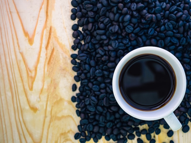 Schwarzer Kaffee in der weißen Schale und im Röstkaffeesamen mit hölzernem Hintergrund.