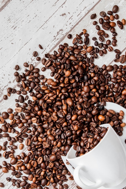 Schwarzer Kaffee in der weißen Schale und in den Kaffeebohnen auf hellem hölzernem Hintergrund.