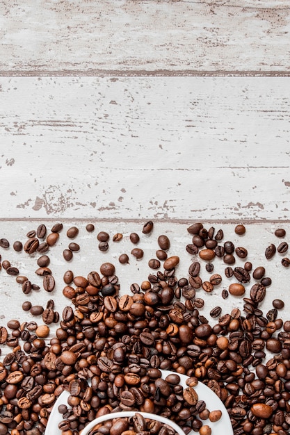 Schwarzer Kaffee in der weißen Tasse und in den Kaffeebohnen auf hellem hölzernem Hintergrund. Draufsicht, Platz für Text