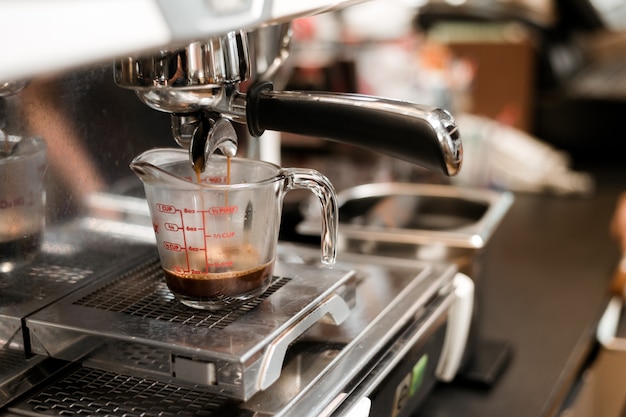 schwarzer Kaffee in Messbecher auf Kaffeemaschine setzen