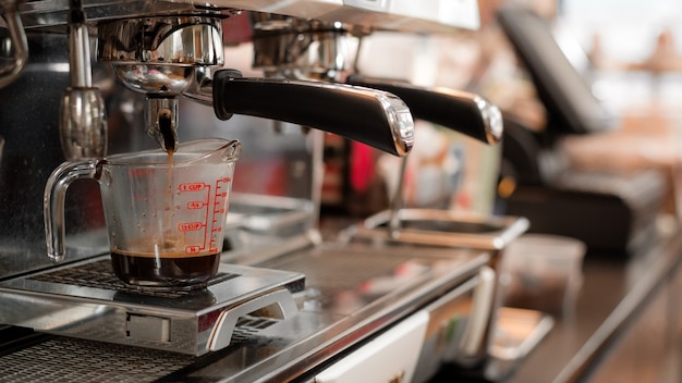 schwarzer Kaffee in Messbecher auf Kaffeemaschine setzen