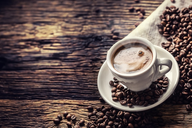 Schwarzer Kaffee in Porzellantasse mit verstreuten Bohnen auf rustikalem Holztisch.