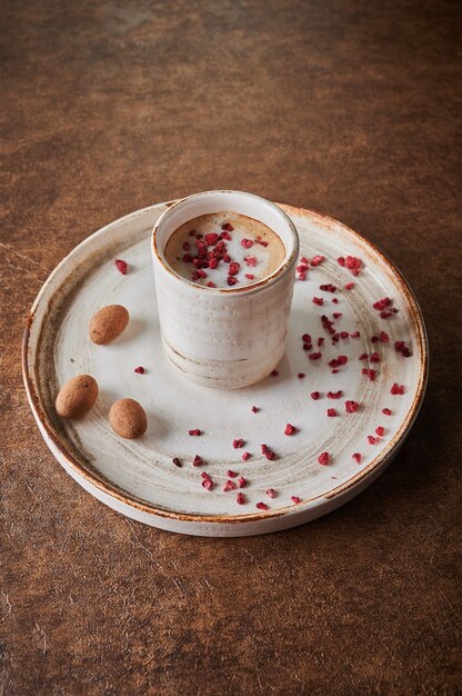 Schwarzer Kaffee mit sublimierten Himbeeren in einem Keramikbecher auf einem Teller in der Nähe von Süßigkeiten Kakaobohnen in