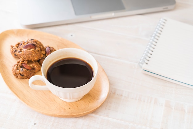 schwarzer Kaffee und Kekse mit Laptop und Notizbuch