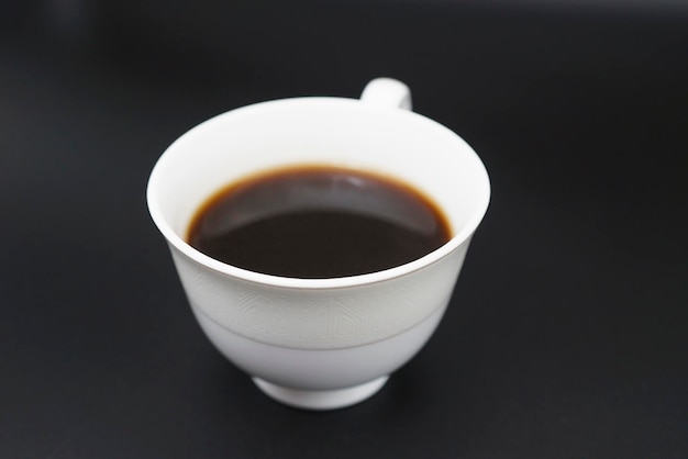Schwarzer Kaffee wird in eine Kaffeetasse aus Porzellan auf schwarzem Hintergrund gegossen