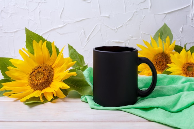 Schwarzer Kaffeebecher mit Sonnenblumen und grüner Serviette auf dem Holztisch Leerer Becher für Markenwerbung