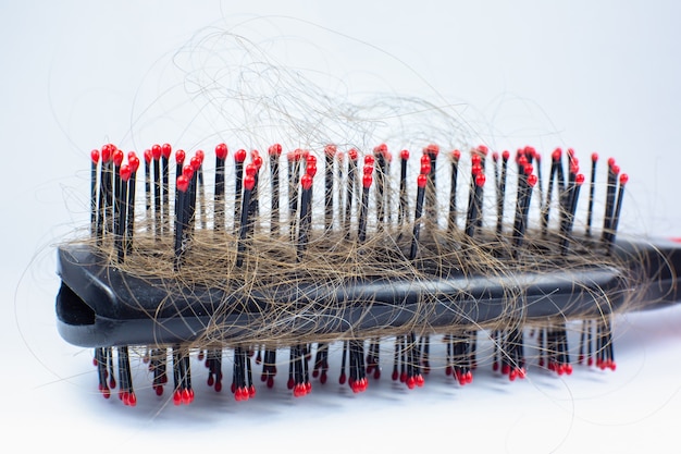 Schwarzer Kamm mit Haaren auf weißem Hintergrund. Problem mit Haarausfall. Nahaufnahme. Betontes Konzept.