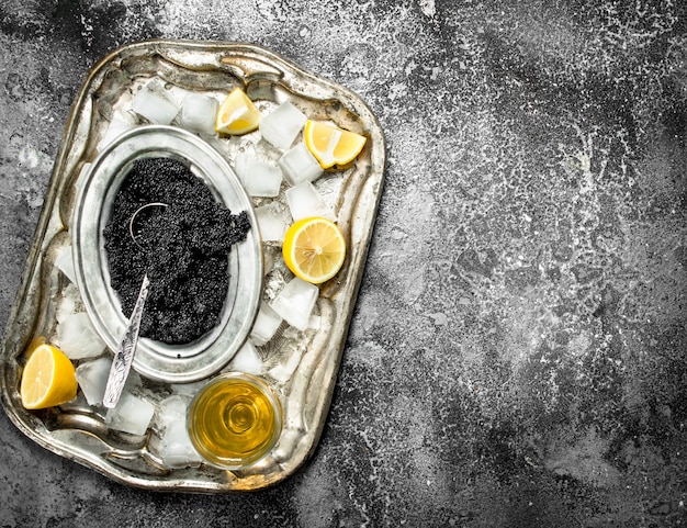 Schwarzer Kaviar mit Weißwein und Zitronenscheiben auf rustikalem Tisch.