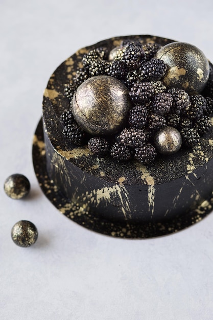 Schwarzer Kuchen mit Brombeeren und goldenen Kugeln dekoriert Festliches Dessert mit Beeren