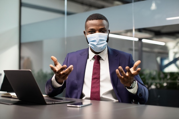 Schwarzer Manager mit Gesichtsmaske, der im Büro arbeitet und eine Konferenz hat
