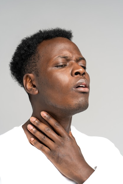 Schwarzer Mann berührt Finger von Halsschmerzen, Schilddrüse isoliert auf grauem Hintergrund.
