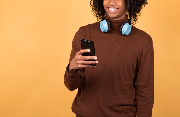 Schwarzer Mann, der jemandem eine SMS schreibt, Freizeitkleidung trägt und isoliert im Studio mit Kopierraum lächelt