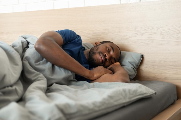 Schwarzer Mann, der mit einer Decke bedeckt schläft, die im Schlafzimmer drinnen ruht