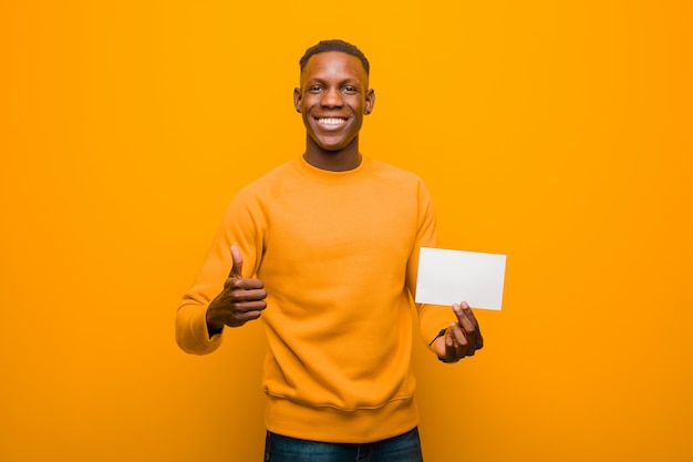 Schwarzer Mann des jungen Afroamerikaners gegen die orange Wand, die ein Plakat wholding ist