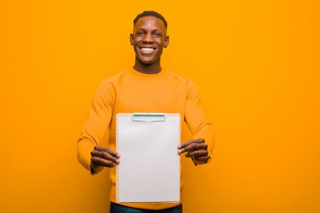 Schwarzer Mann des jungen Afroamerikaners gegen die orange Wand, die ein Plakat wholding ist