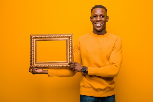 Schwarzer Mann des jungen Afroamerikaners gegen orange Wand mit einem Barockrahmen