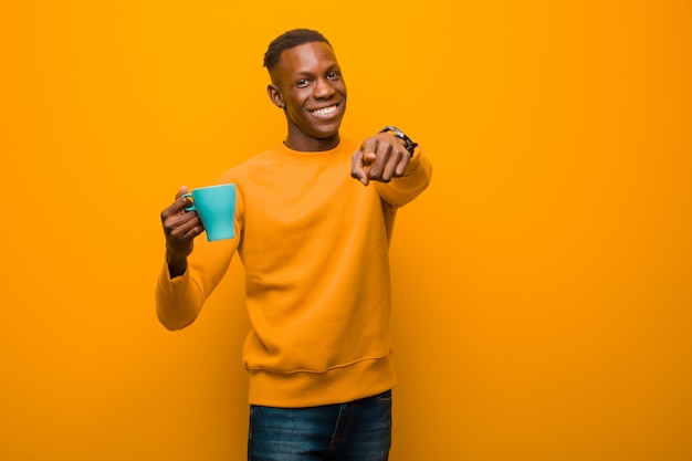 Schwarzer Mann des jungen Afroamerikaners gegen orange Wand mit einer Kaffeetasse