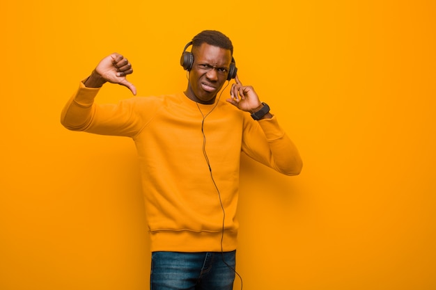 Schwarzer Mann des jungen Afroamerikaners gegen orange Wand mit Kopfhörern