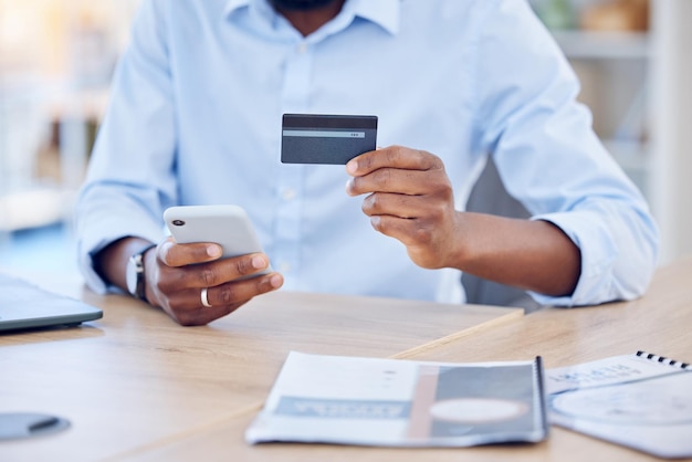 Schwarzer Mann hält Kreditkarte und Smartphone für E-Commerce und Fintech-Unternehmenszahlung und Bank-App in der Hand. Männlicher Berufstätiger im Büro mit Geschäftseinkäufen, Online-Shopping und Internet-Banking