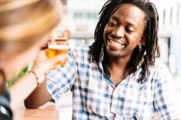 Schwarzer Mann mit Dreadlocks, die mit einem Bier anstoßen